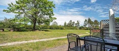 Eine Terrasse im Freien mit Tisch und Stühlen, einem Baum und einer Hecke.