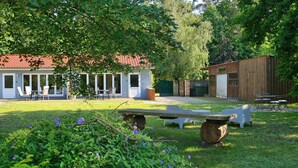 Una casa con techo de tejas rojas, un patio con mobiliario exterior y un jardín con banca de madera y plantas.