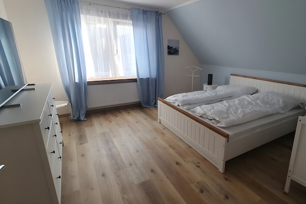 Un dormitorio con cama, cómoda, radiador, ventana con cortinas y mesita de noche.