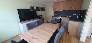 Una cocina compacta con una mesa y sillas, un televisor de pantalla plana, armarios de madera y una cafetera.