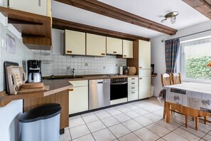 Una cocina con armarios de madera, lavavajillas, cafetera y un comedor con mesa y sillas.