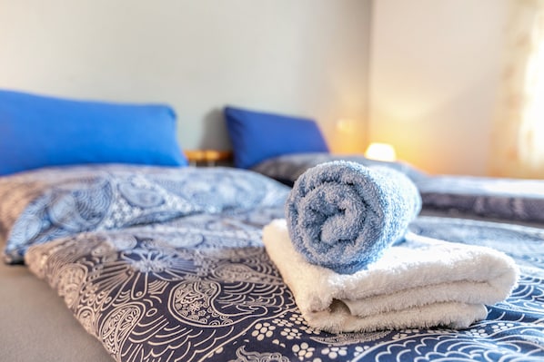 A neatly made bed with patterned bedding and rolled towels.