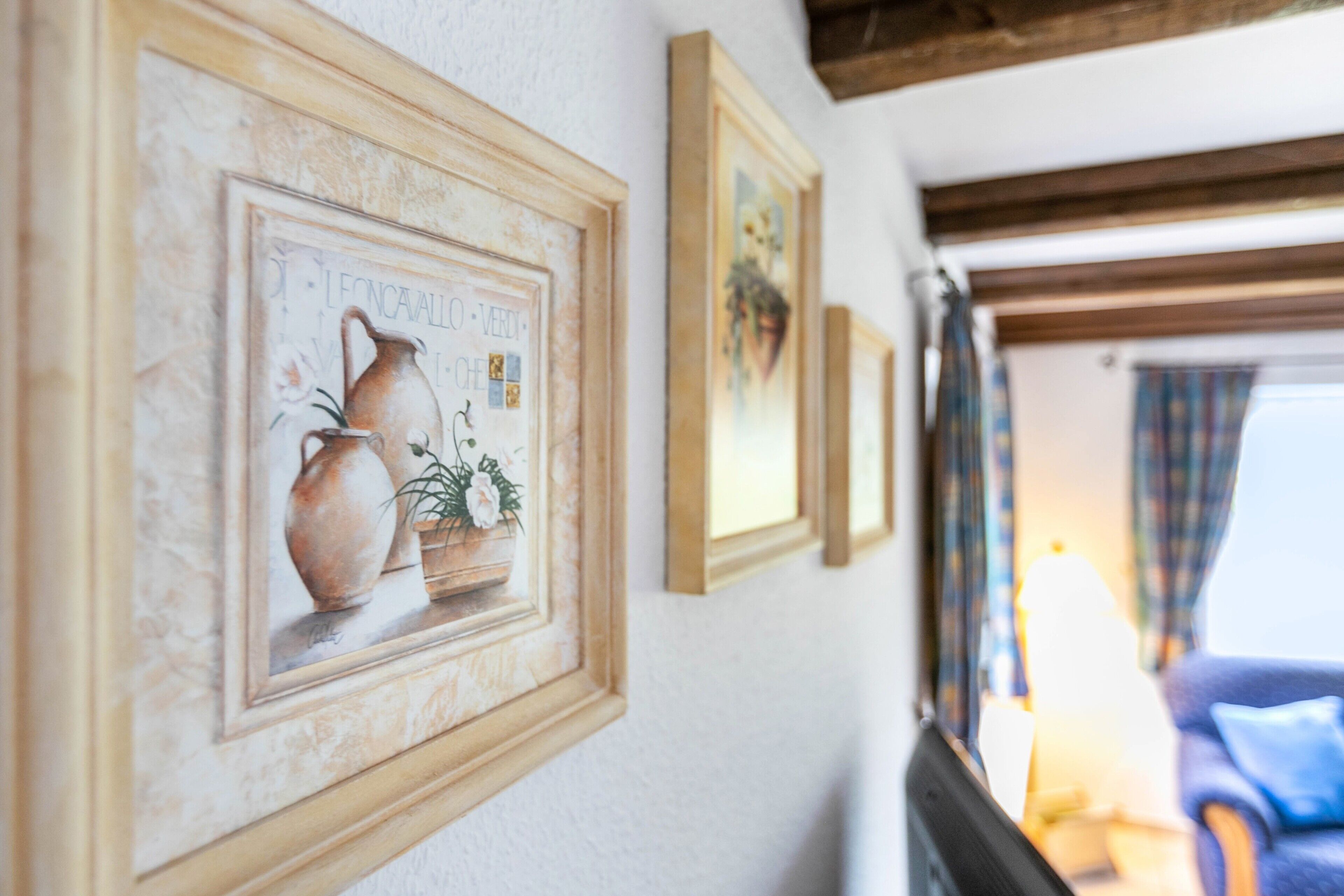 A hallway with framed artwork on the wall, a lamp, and a blue chair.