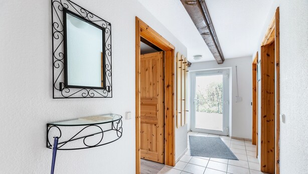 A hallway with a mirror, a wall-mounted light fixture, and wooden doors leading to a balcony. - Apartment 'Haus Schröder' with Shared Terrace, Shared Garden and Wi-Fi (Sankt Michaelisdonn)