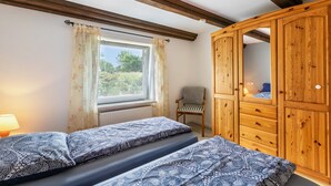 A bedroom with two beds, a wooden wardrobe, a chair, and a window with curtains. - Apartment 'Haus Schröder' with Shared Terrace, Shared Garden and Wi-Fi (Sankt Michaelisdonn)