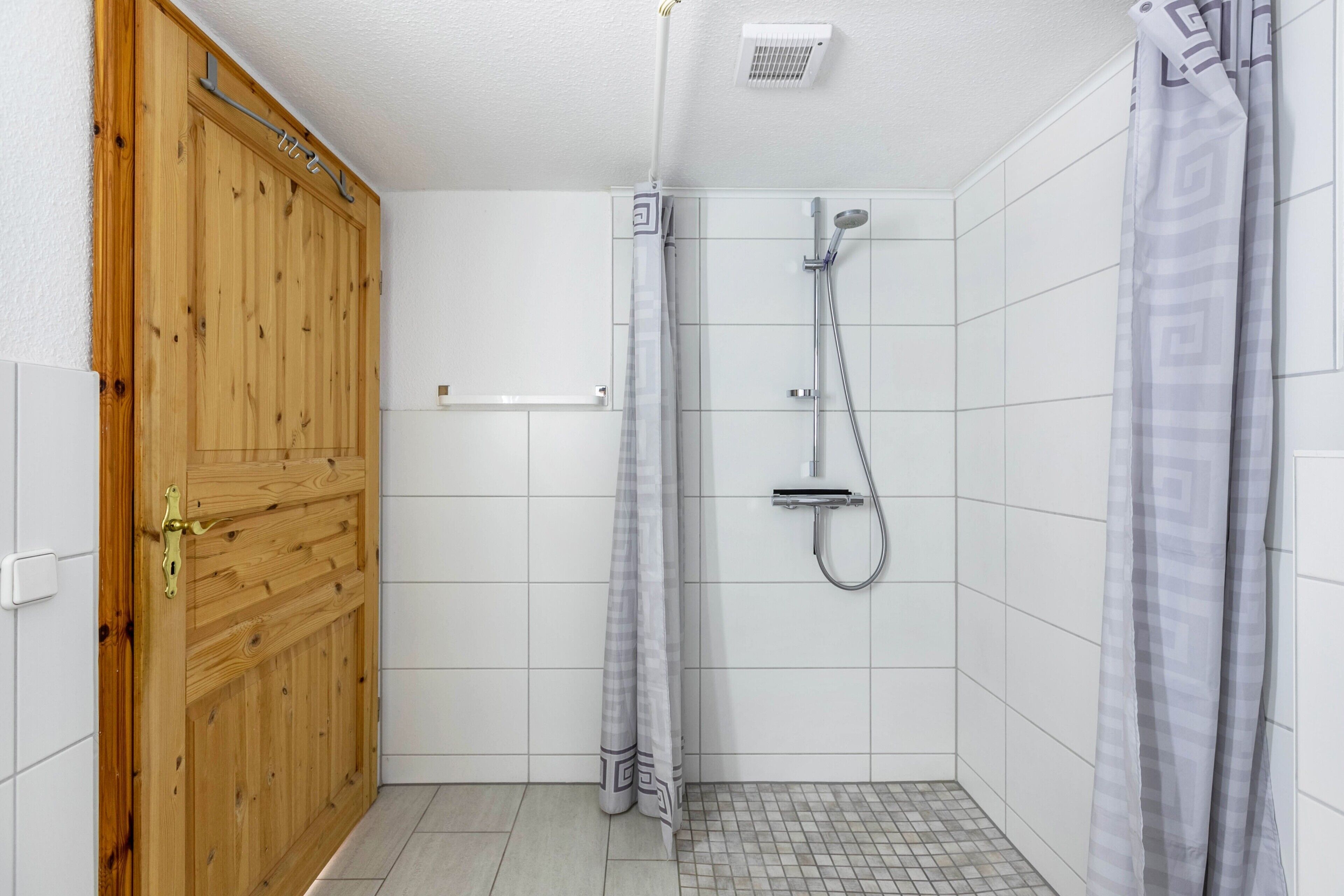 A shower with a handheld showerhead, a towel rack, and a wooden door.
