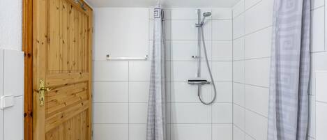 A shower with a handheld showerhead, a towel rack, and a wooden door.