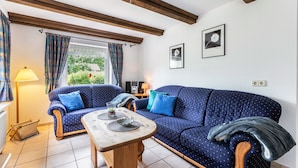A cozy living room with a blue sofa, wooden table, and a view of greenery outside. - Apartment 'Haus Schröder' with Shared Terrace, Shared Garden and Wi-Fi (Sankt Michaelisdonn)