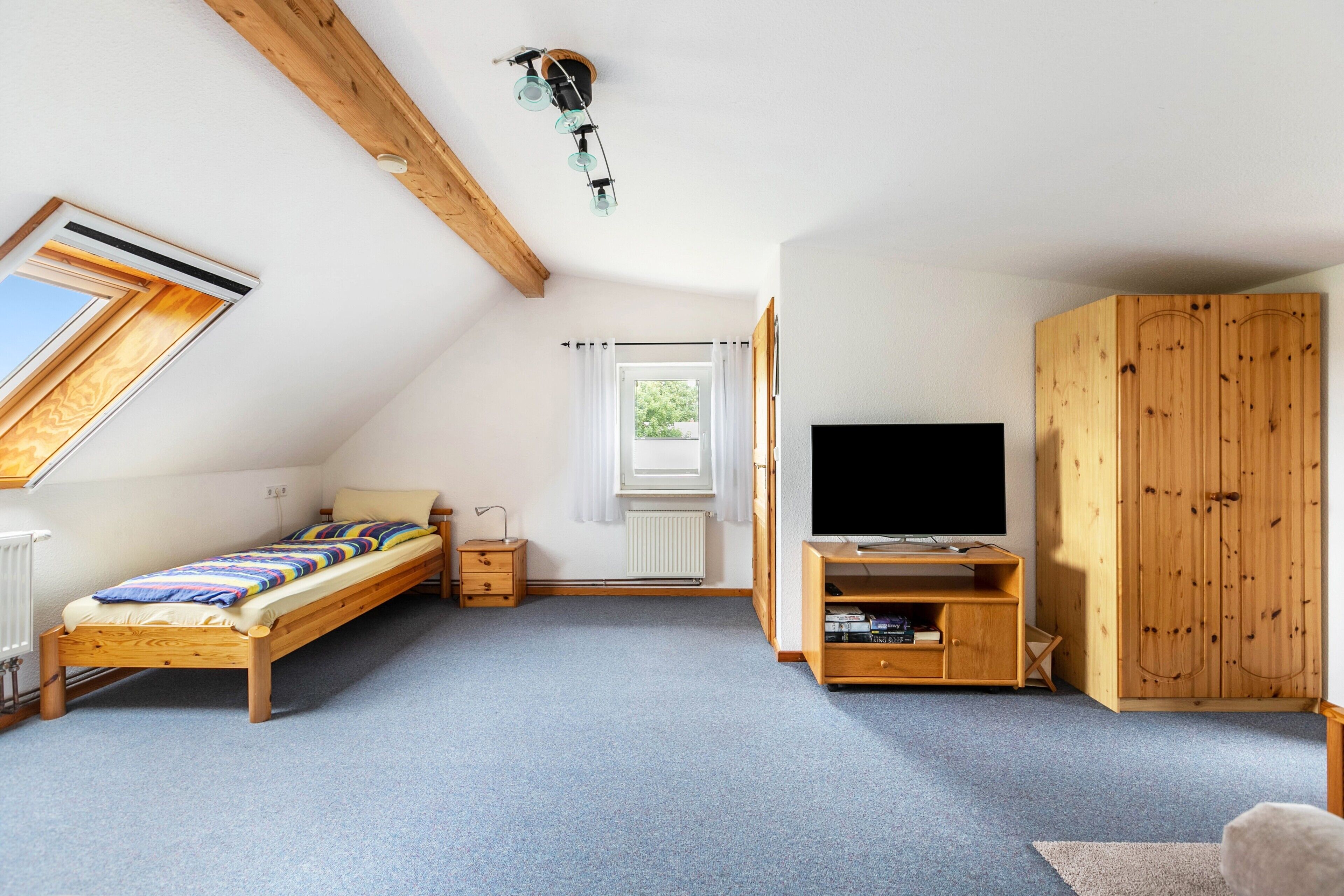 Une chambre avec un plafond en pente, un lit, un meuble pour la télévision, une armoire et une fenêtre.