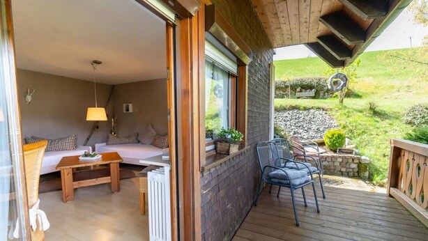 Ein gemütliches Zimmer mit einer Couch, einem Tisch und einem Stuhl, eine Holzterrasse mit Blick auf den Garten.