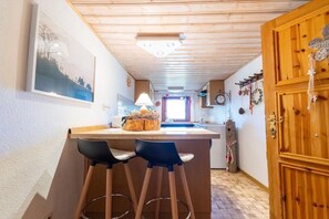 A kitchen with wooden cabinets, a bar area with stools, a hanging light fixture, and a window with decorations.