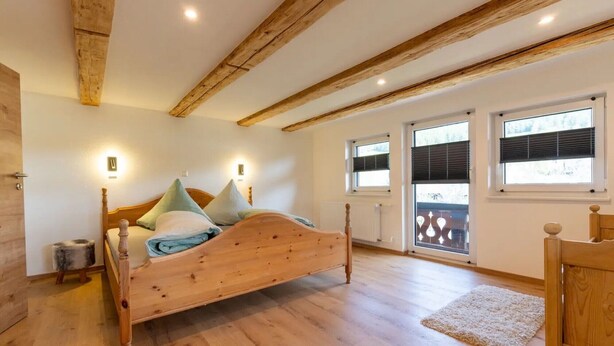 A bedroom with a wooden bed, two windows with blinds, a radiator, and a wooden floor.