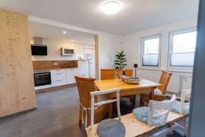 A modern kitchen with white cabinets, a microwave, and a dining area with a wooden table and wicker chairs.