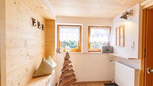 A cozy cabin room with wooden walls, a small staircase, two windows with curtains, a radiator, and a door.