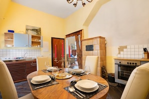 A dining room with a wooden table set for four, a kitchen with a stove, and a dining area with chairs. - Holiday Apartment 'Wohnen Im Alten Rittergut' with Private Terrace, Private Garden and Wi-Fi (Calau)