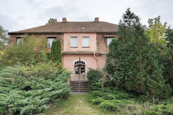 Une maison à deux étages avec une porte d’entrée, un escalier menant à l’entrée et un jardin agrémenté de divers arbustes et arbres.