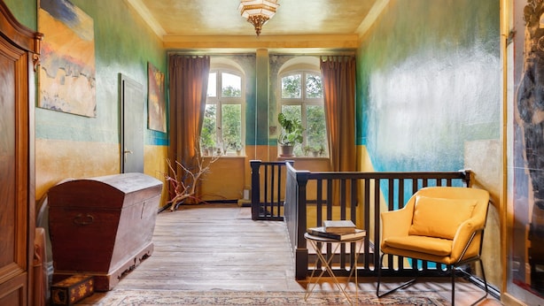 A room with a wooden chest, a yellow armchair, a small table, and a chandelier. - Apartment 'Wohnen Im Alten Rittergut' with Private Terrace, Garden & Wi-Fi (Calau)