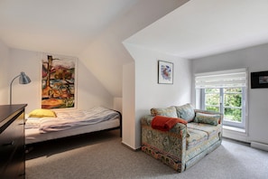 Ein Schlafzimmer mit Bett, Sofa, Schreibtisch, Lampe, Gemälde und einem Fenster.