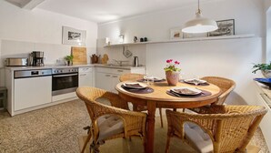 A kitchen with white cabinets, a dining table with wicker chairs, and a hanging pendant light.