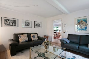 Ein Wohnzimmer mit zwei dunklen Sofas, einem Glastisch und gerahmten Kunstwerken an den Wänden.