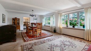 A dining area with a table and chairs, a wooden chest, and a window with curtains.