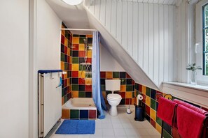 Casa de banho com chuveiro, sanita e janela.