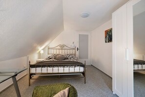 Quarto com cama, cadeira, mesa de cabeceira, porta e um quadro na parede.