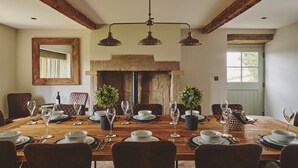 A dining room with a wooden table set for a meal, a stone fireplace, and a large mirror on the wall. - Rye Top Farm - Luxury Cottages (Uppermill)