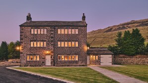 A two-story stone building with multiple windows and a small attached garage. - Rye Top Farm - Luxury Cottages (Uppermill)