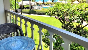 Un balcone con mobili in vimini che si affaccia su una zona piscina con palme e vista sull'oceano.