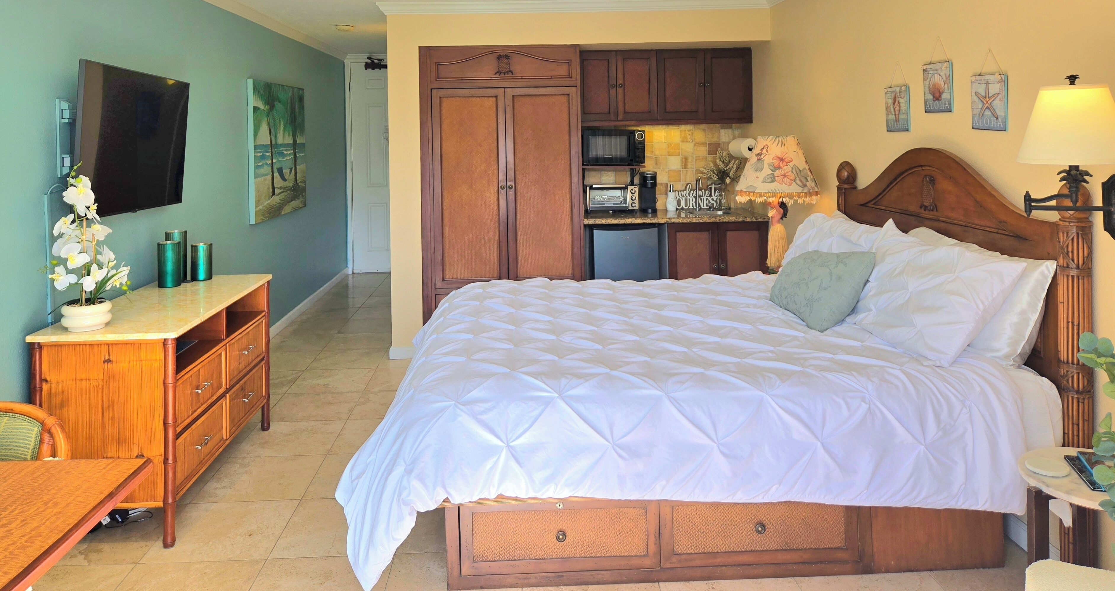 Un dormitorio con una cama grande, un armario de madera, una pequeña cocina americana y un comedor.