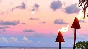 Una spiaggia con due torce infuocate, un cartello e l'oceano sullo sfondo.
