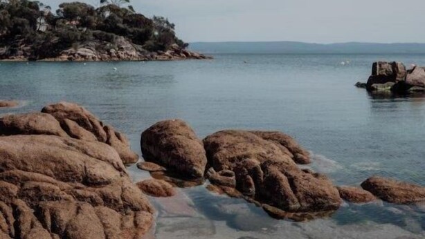 En stenig kustlinje med klart vatten och land i fjärran.