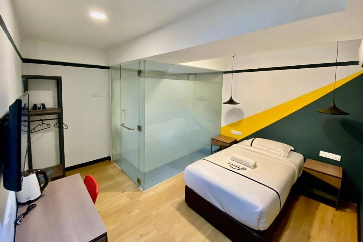 Een moderne hotelkamer met een bed, een bureau, een stoel, een kledingkast en een douchecabine met glazen wanden.