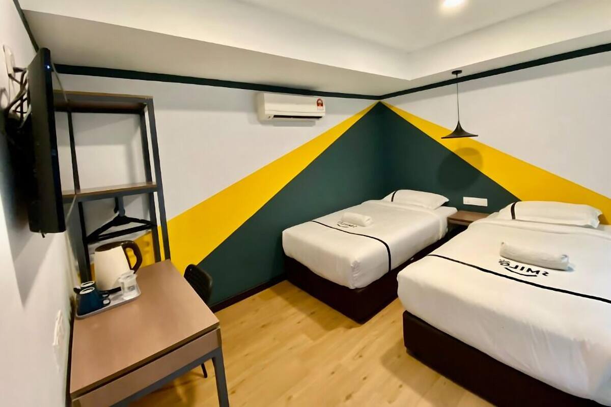 Een hotelkamer met twee bedden, een kleine tafel, een plankje met toiletartikelen en een wandontwerp met geometrische patronen.