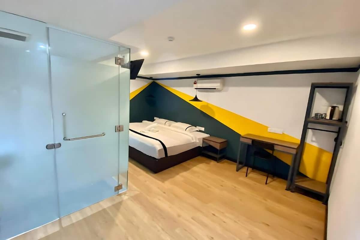 Een moderne slaapkamer met een glazen kledingkast, een bed met witte beddengoed, een bureau met stoel en een klein tafeltje met lamp.
