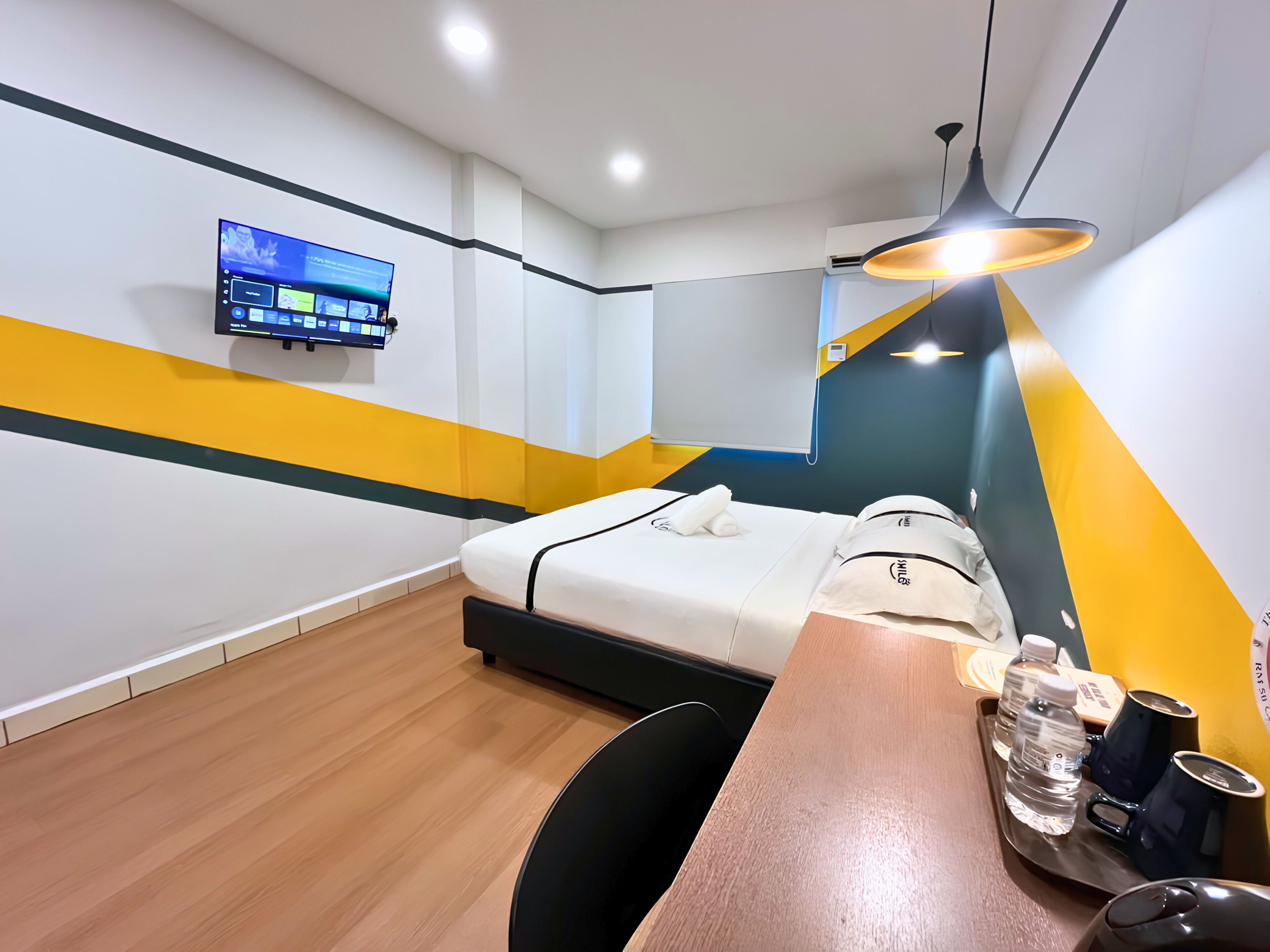 Habitació d'hotel amb un llit, escriptori, cadira, televisió penjada a la paret i un lluminari al sostre.