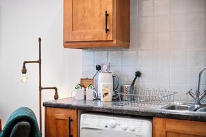 A kitchen with wooden cabinets, a coffee maker, a dish rack, and a dishwasher.