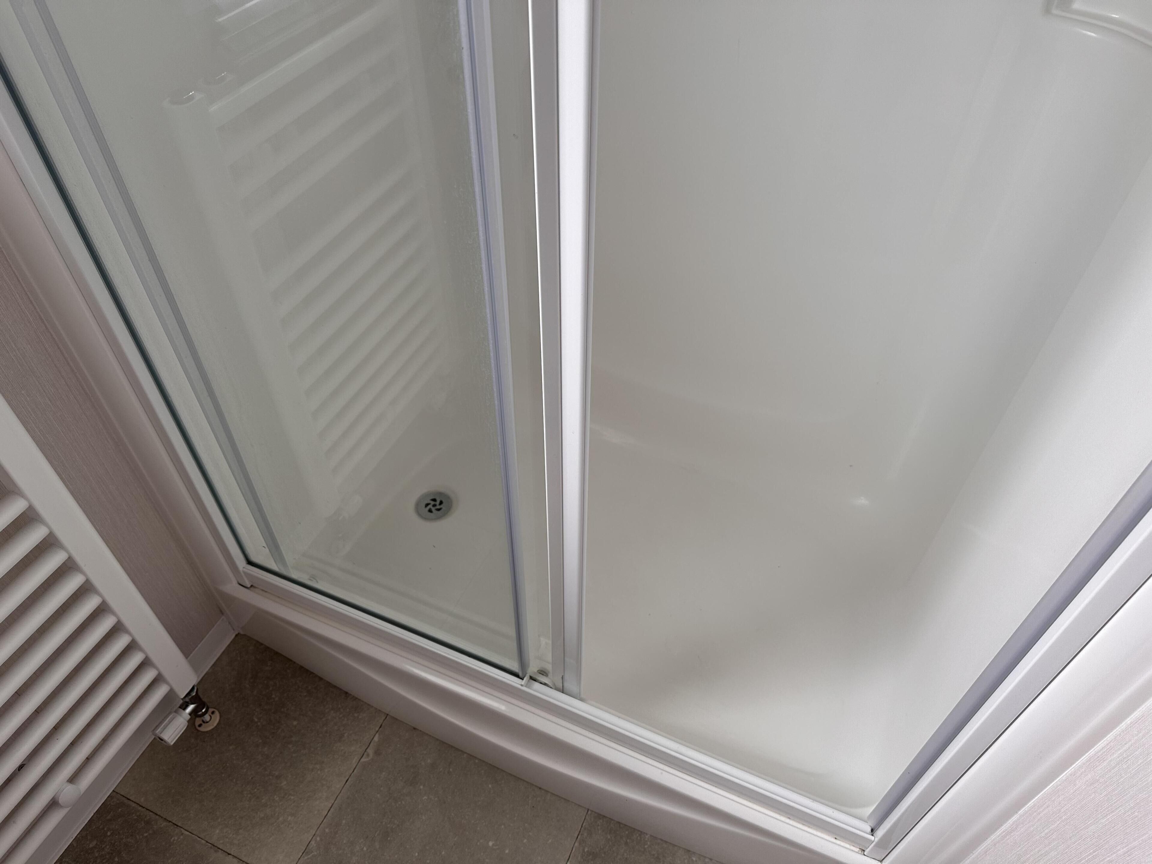 A glass shower enclosure with a white frame and a drain in the center.