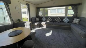 Un interior de autocaravana acogedor, con un sofá modular, una mesa redonda y una pequeña zona de estar.