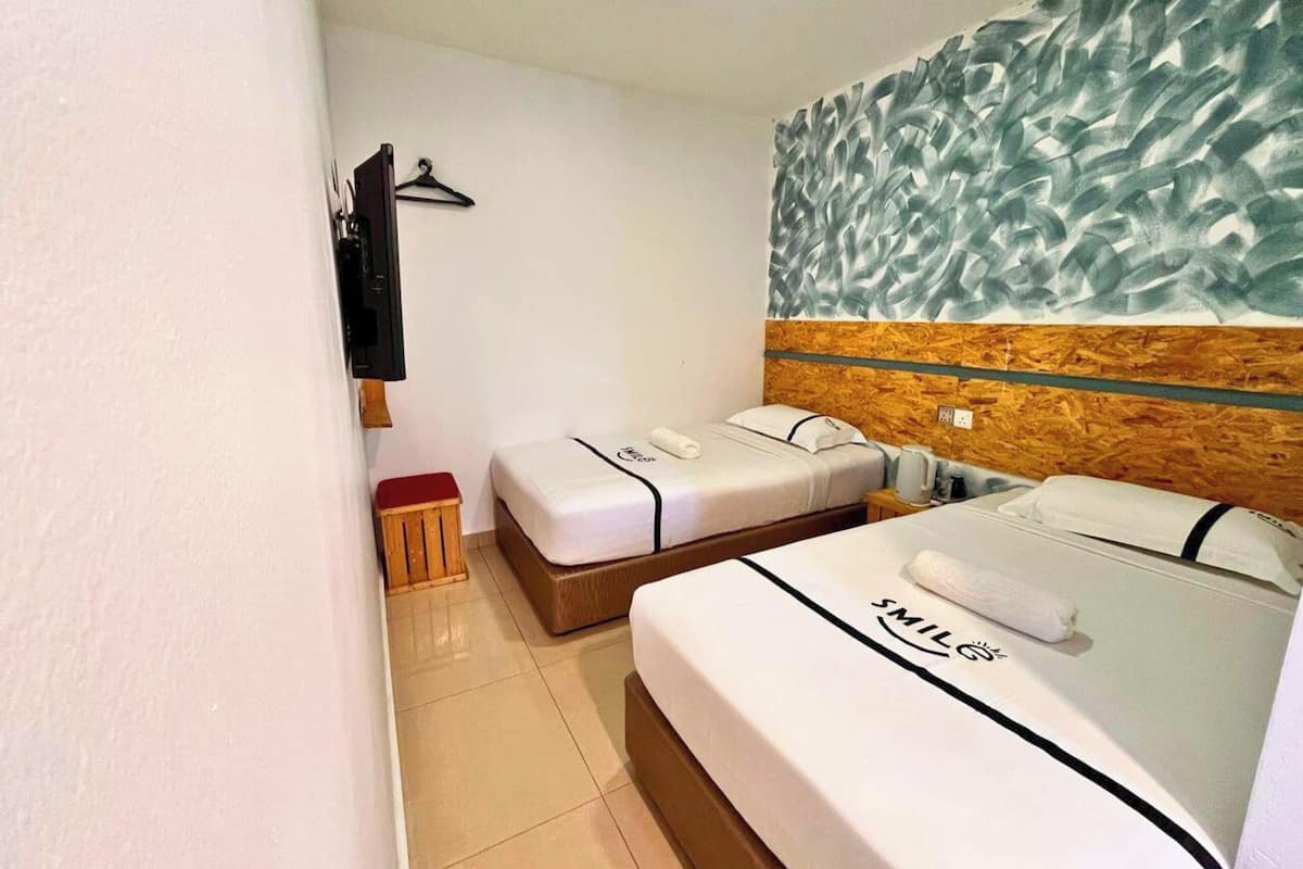A hotel room with two beds, a wooden headboard, a wall-mounted TV, and a small wooden stool.
