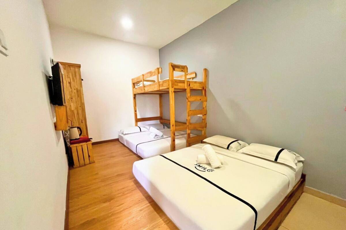 A small, compact room with a bunk bed, a single bed, a wooden cabinet, and a television.