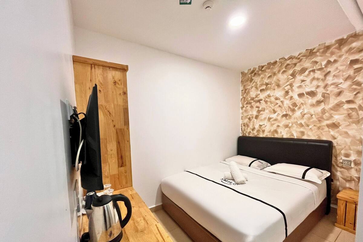A small, clean room with a bed, a wooden cabinet, and a textured wall.