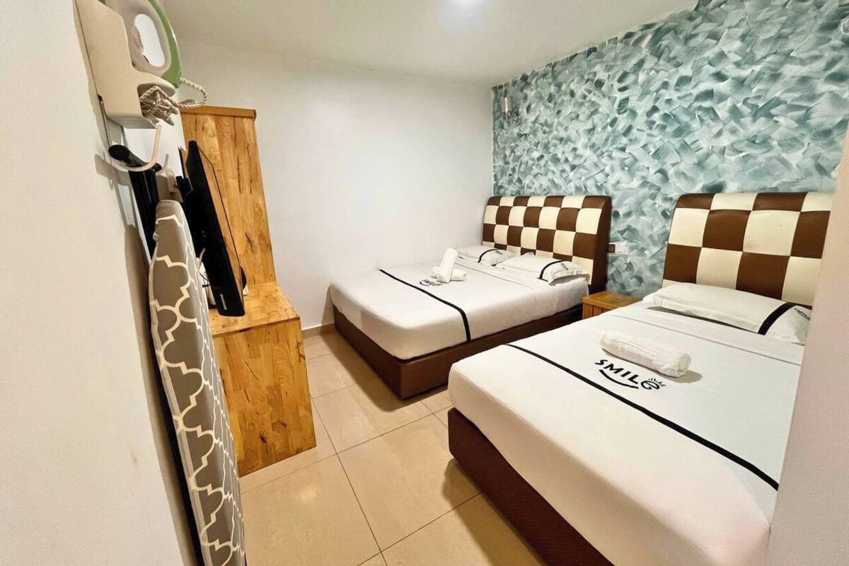 A hotel room with two beds, a wooden cabinet, and a textured wall.