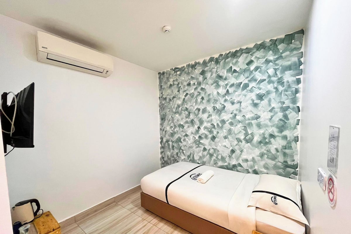 A small, modern room with a bed, a wall-mounted air conditioner, and a textured wall.