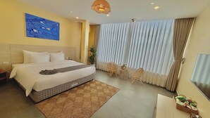 A hotel room with a large bed, a desk with a computer, a TV, a window with curtains, and a painting on the wall. - Truong Giang Boutique Hotel (Thao Nguyen)
