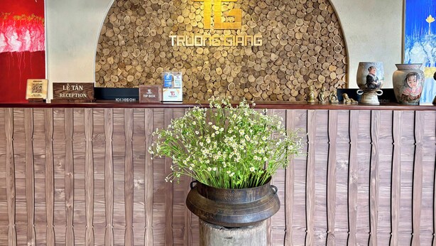 A reception desk with a wooden log wall, a 'TRUONG GANG' sign, a tip box, and a QR code for check-in. - Truong Giang Boutique Hotel (Thao Nguyen)