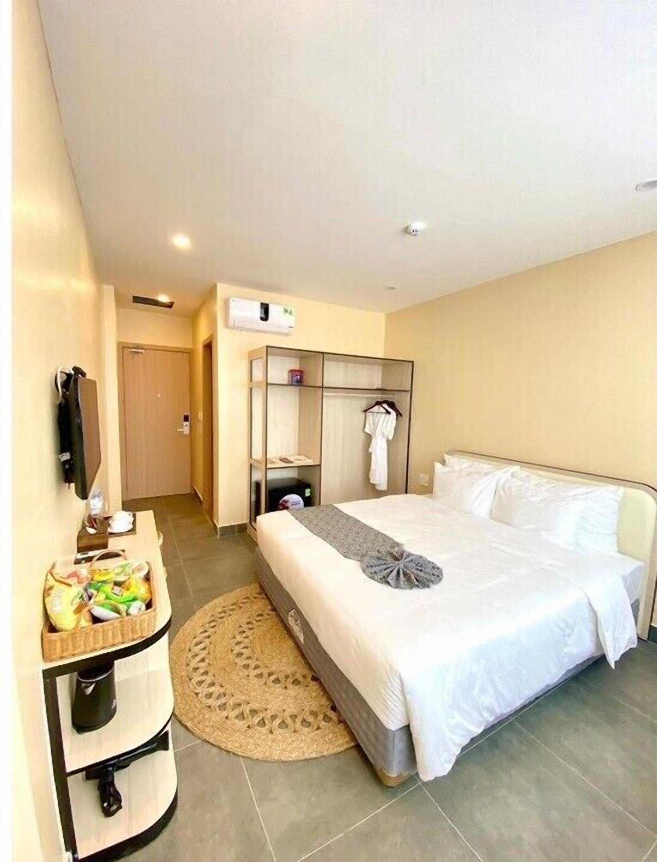 Ein Hotelzimmer mit einem Bett, einem Nachttisch mit Korb, einem Kleiderhaken und einer Wand-Klimaanlage.
