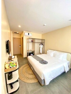 Habitación de hotel con una cama, una mesita de noche con una cesta, un perchero y un aire acondicionado instalado en la pared.