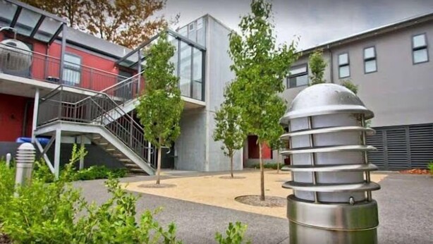 A modern building with a staircase leading to a balcony, surrounded by greenery and a clear sky. - One Bedroom Apartment (Newcastle West)